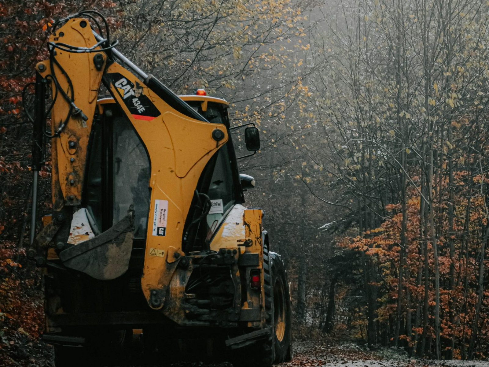A yellow excavator on a foggy autumn forest path, creating a tranquil and eerie scene.